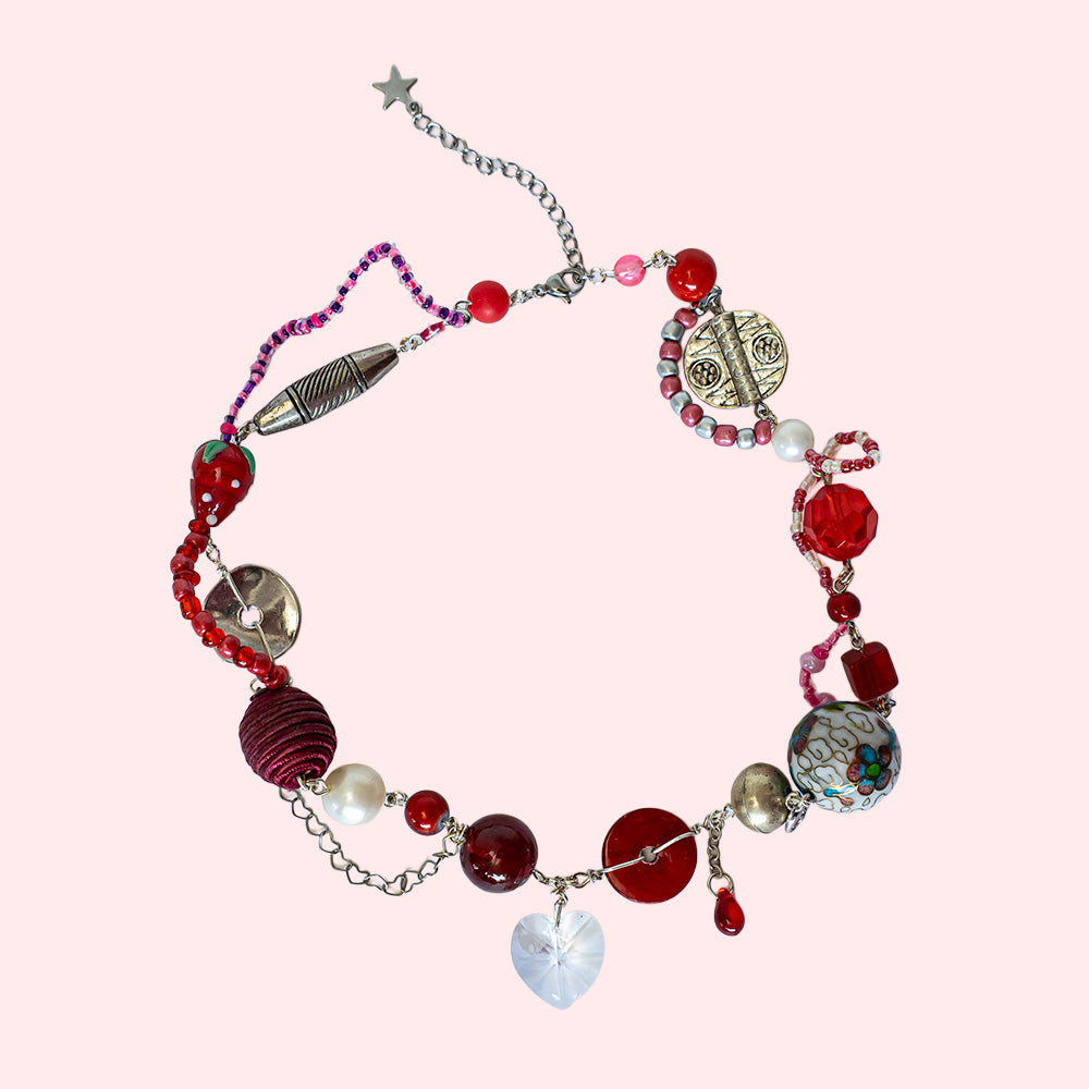 Handmade, colorful (mostly red) necklace in silver and red made with large beads of various materials. In the middle is a glass heart pendant.