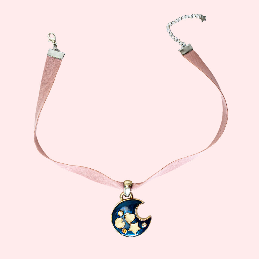 A choker in pink ribbon with a large pendant representing a dark blue moon crescent with small white symbols.