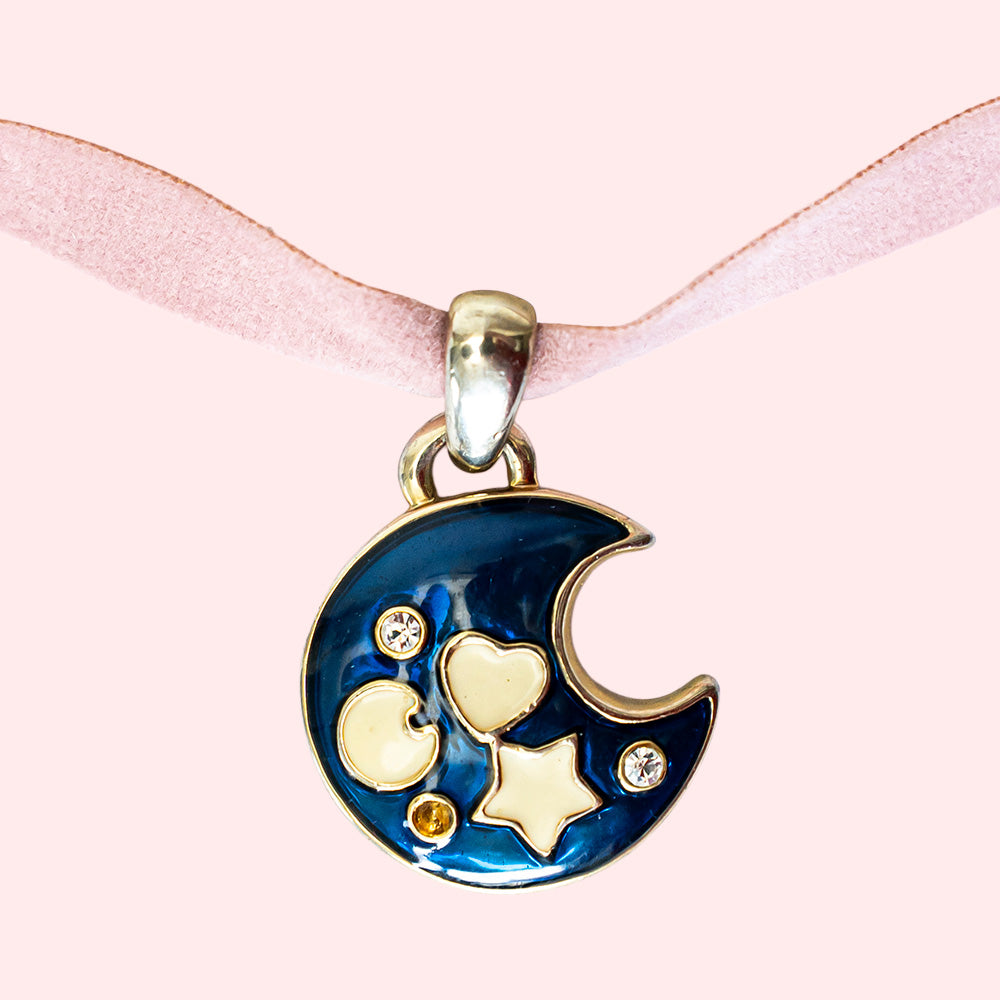 A choker in pink ribbon with a large pendant representing a dark blue moon crescent with small white symbols.