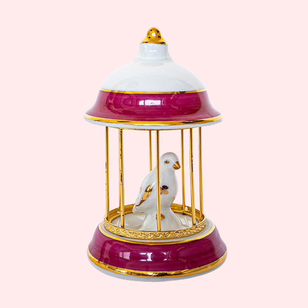 A vintage Limoges porcelain white, golden and red birdcage with a small white and golden bird sitting in it. 