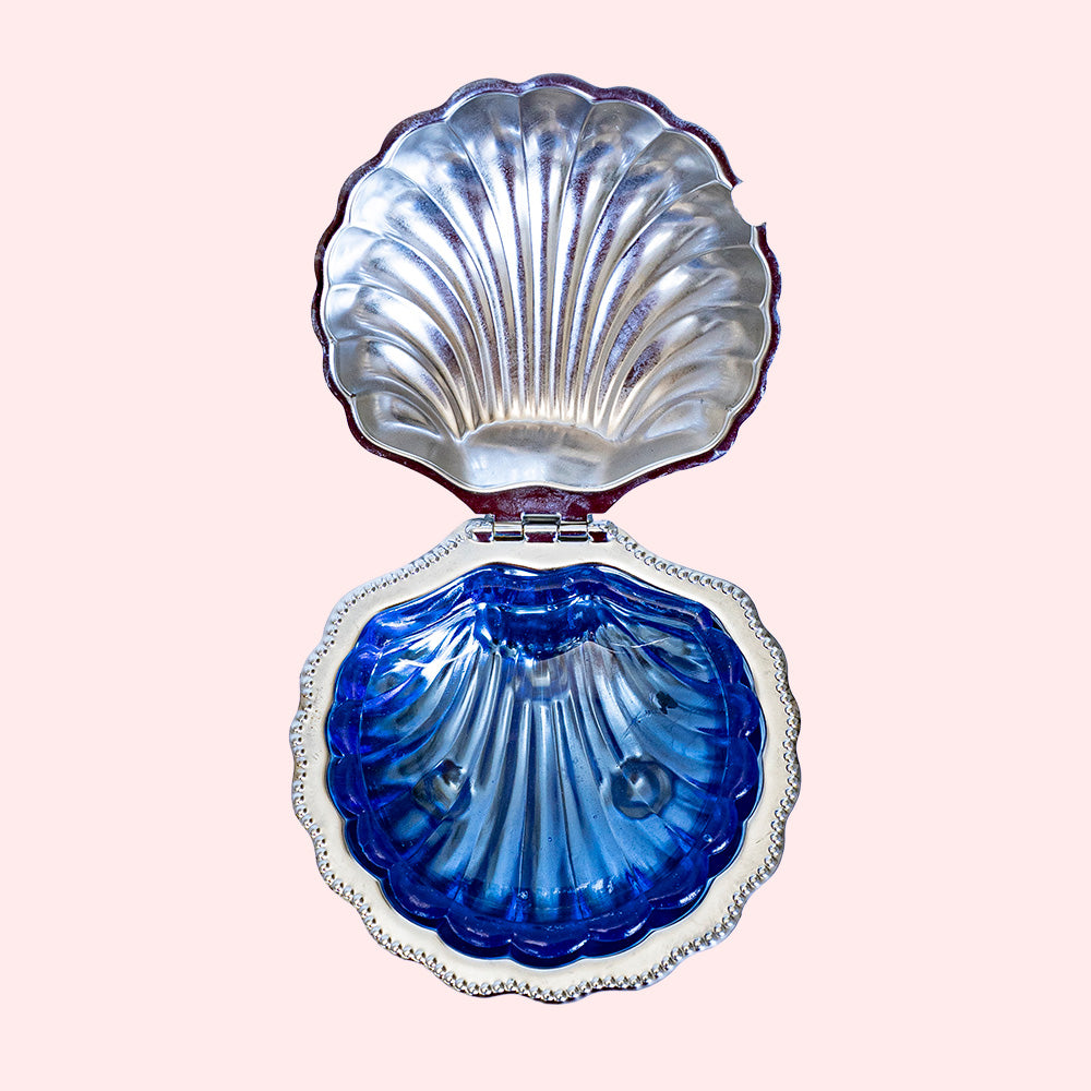 A silver butter dish in the shape of a shell with a blue glass part inside. It can be used as a trinket tray. 