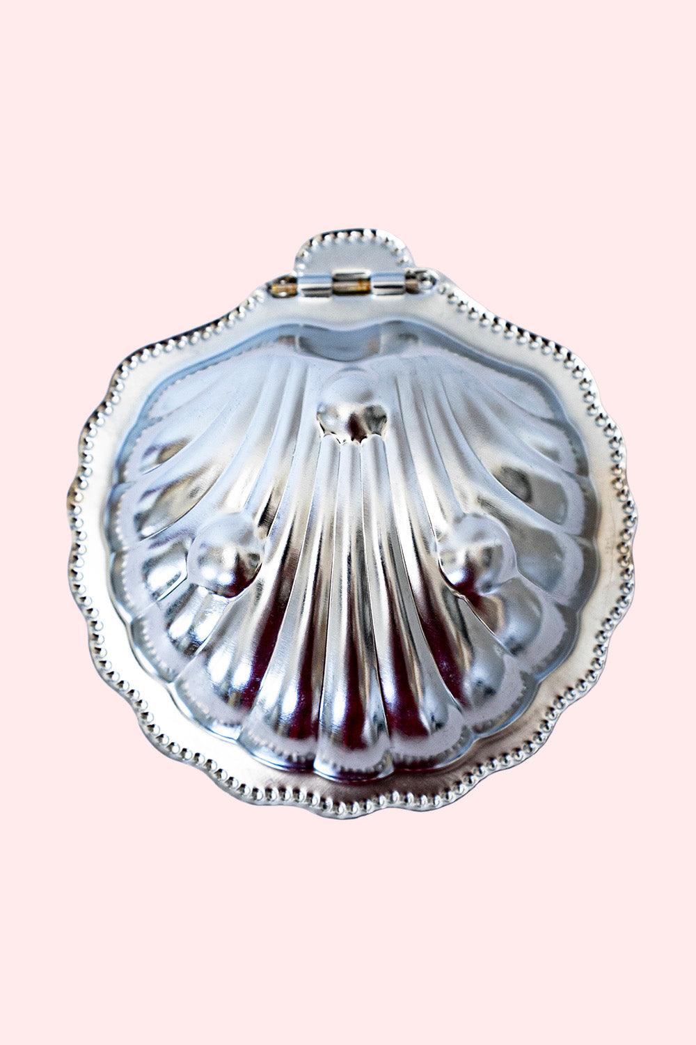 A silver butter dish in the shape of a shell. It can be used as a trinket tray. Seen from under, with three bumps representing the feet. 