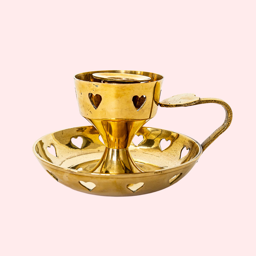 A golden vintage candlestick with heart cutouts around the base and the candle holding part. It also has a heart on top of the handle.