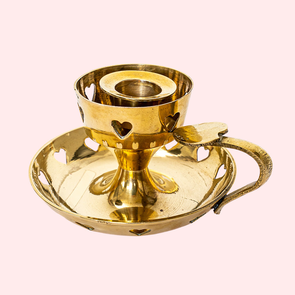 A golden vintage candlestick with heart cutouts around the base and the candle holding part. It also has a heart on top of the handle.