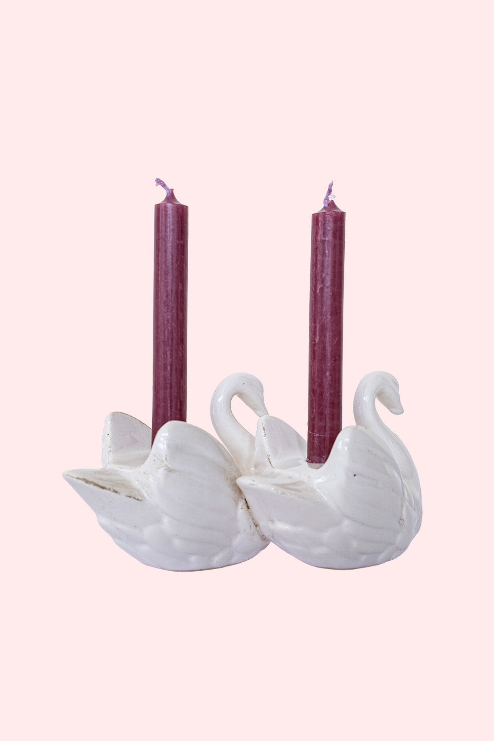A vintage porcelain candlestick in the shape of a couple of swans, each holding a small red candle between their wings.