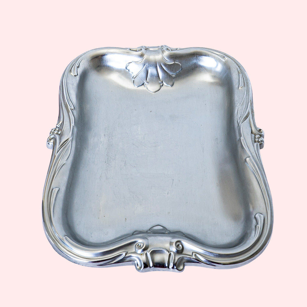 A vintage stainless steel tray with decorative edges.