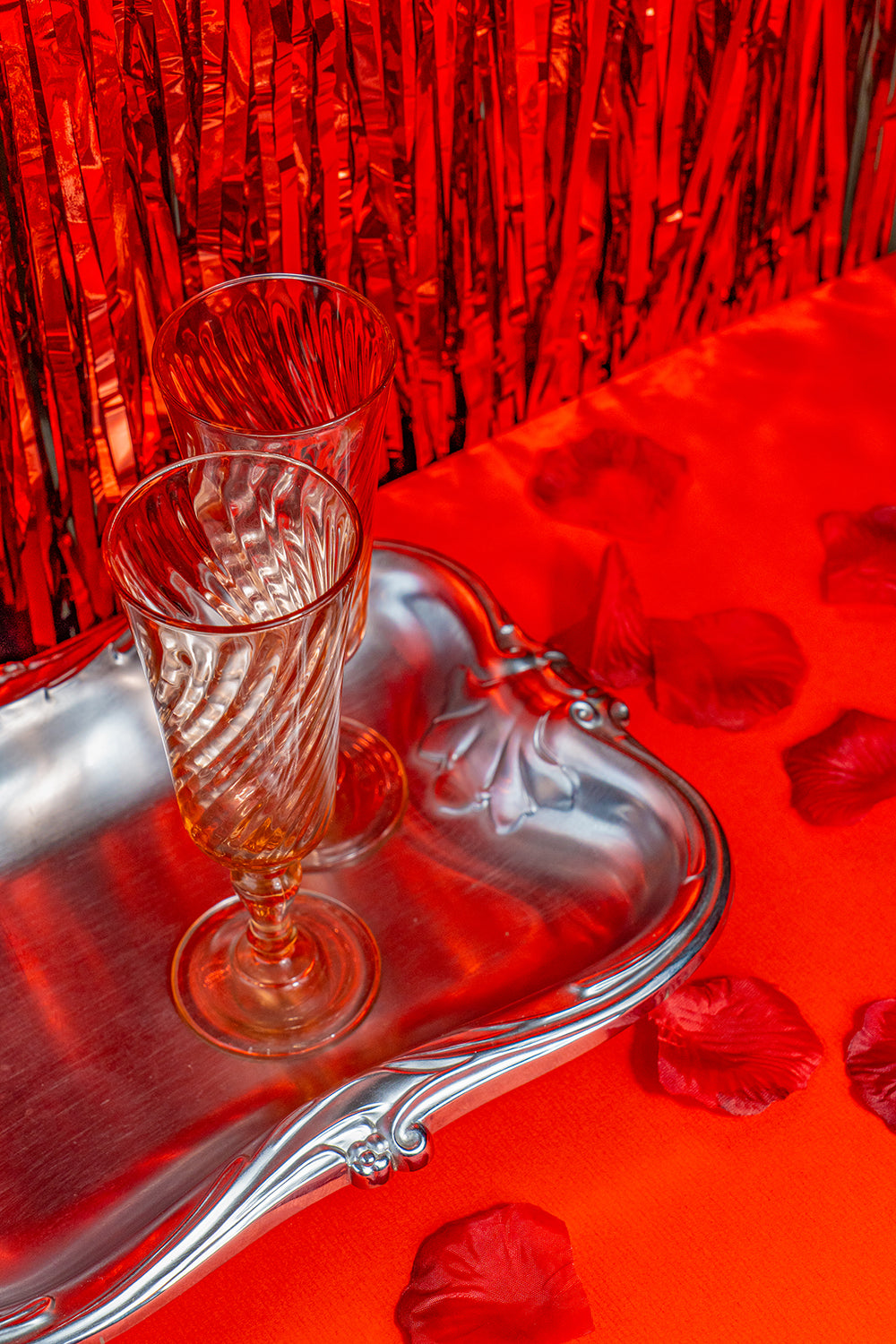 Two pink crystal glasses on a silver tray with a red tinfoil background.