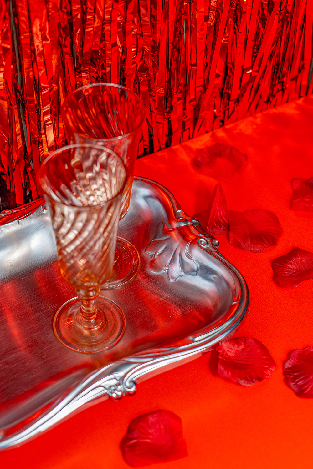 Two pink crystal glasses on a silver tray with a red tinfoil background.