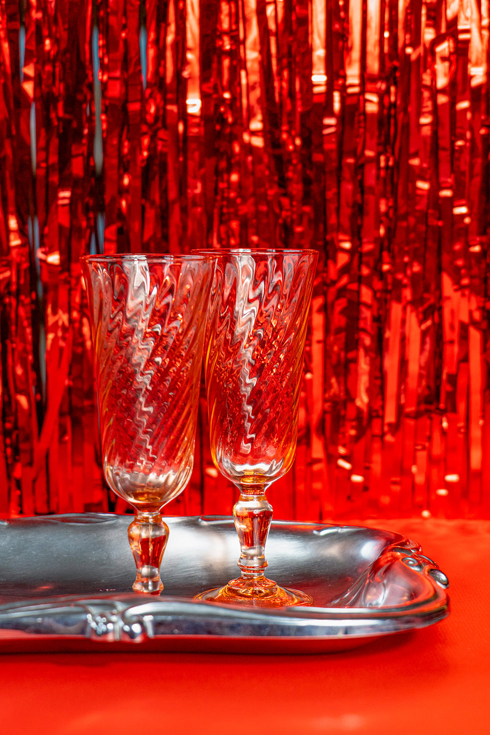 Two pink crystal glasses on a silver tray with a red tinfoil background.