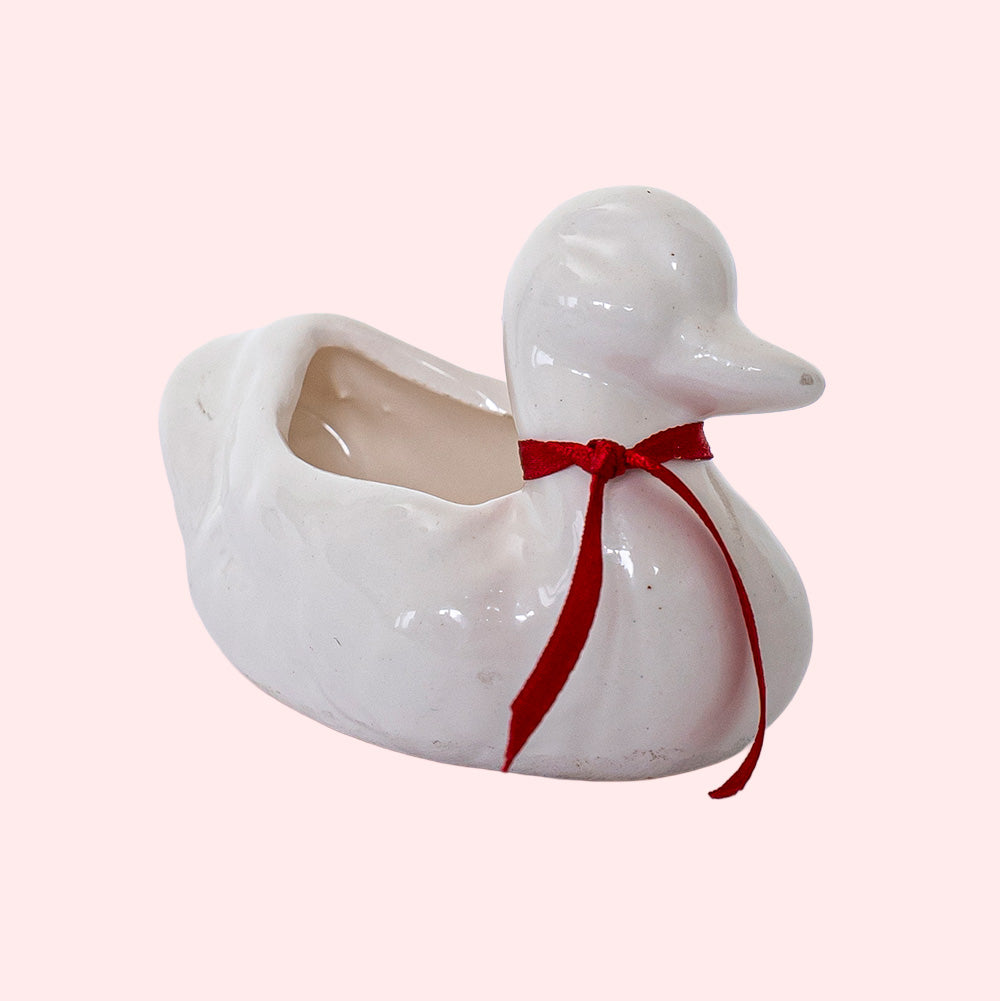 A vintage hollow porcelain duck with a red ribbon around its neck