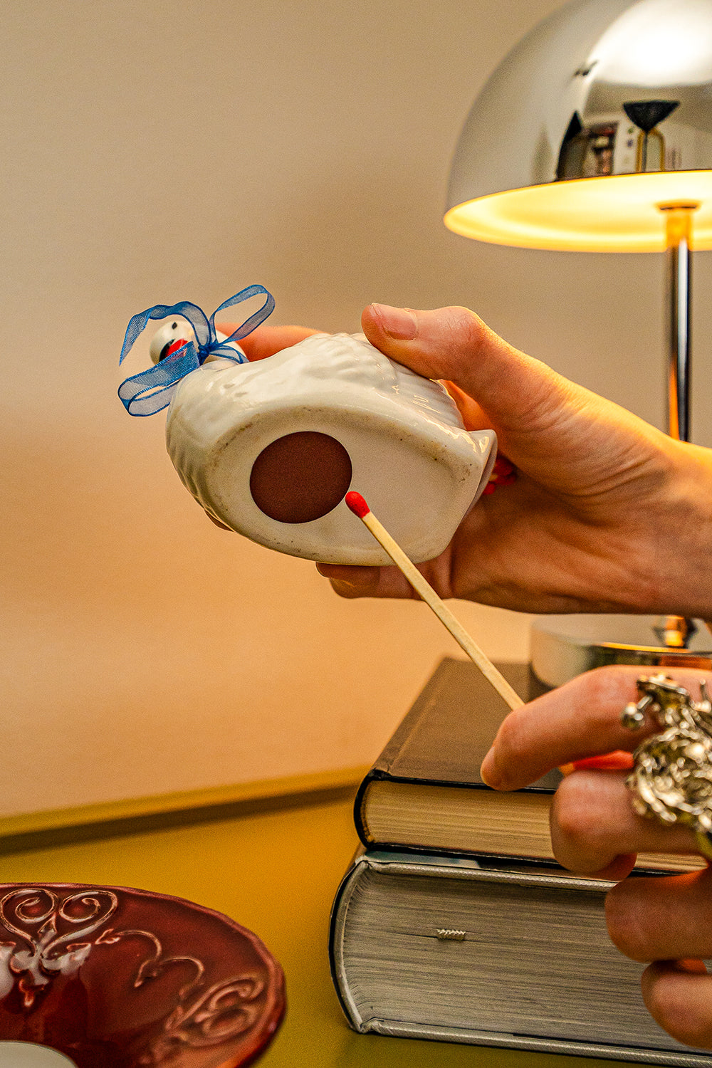 A person about to strike a match on a second hand, ceramic swan figuring that doubles as a match vessel and striker.