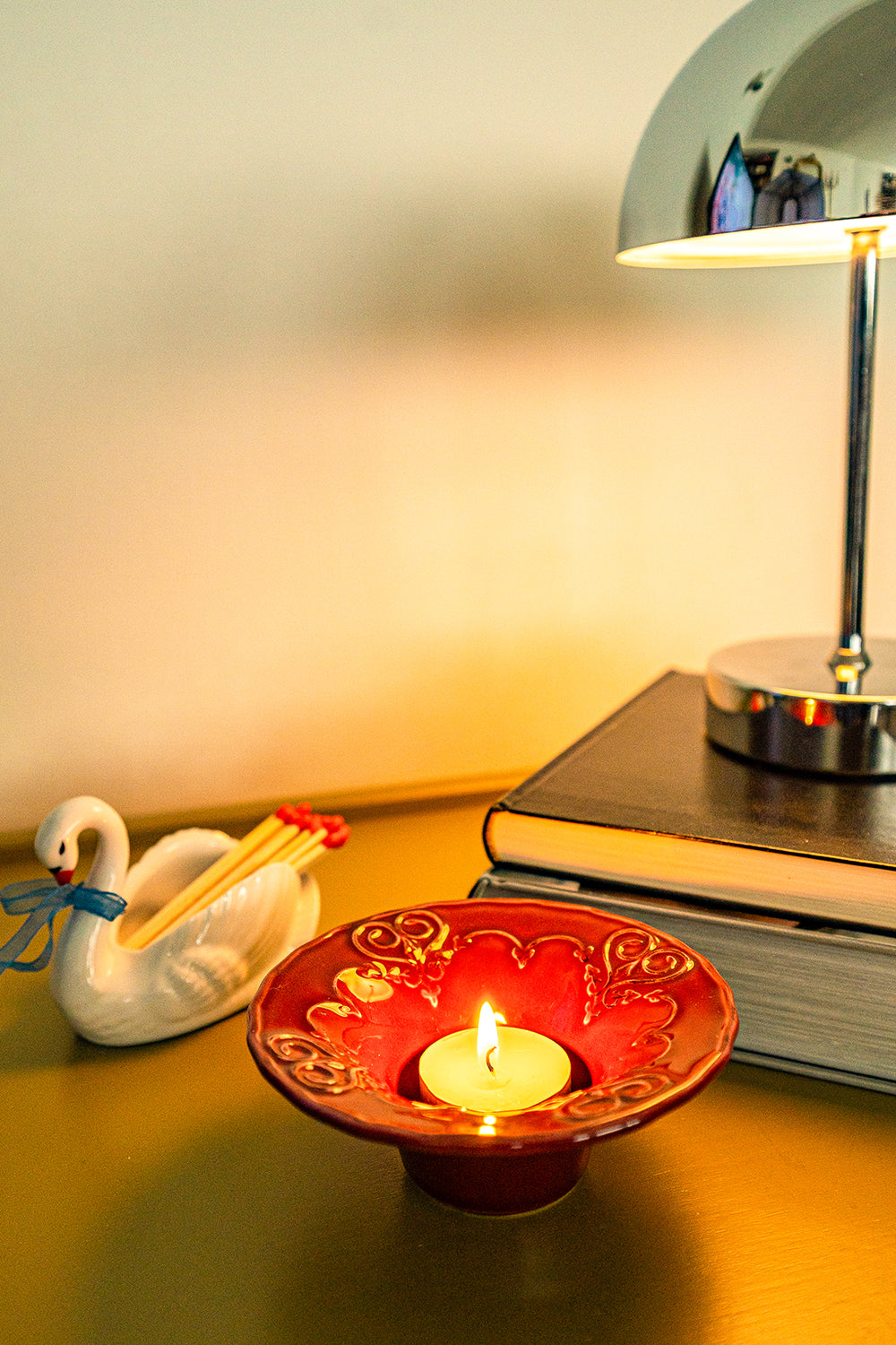 Second hand, ceramic figurine swan with matches on a table next to a red candleholder with a lit tealight.