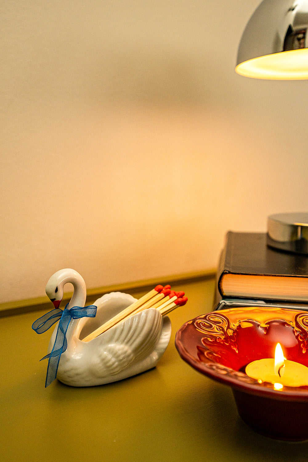 Second hand, ceramic figurine swan with matches on a table next to a red candleholder with a lit tealight.
