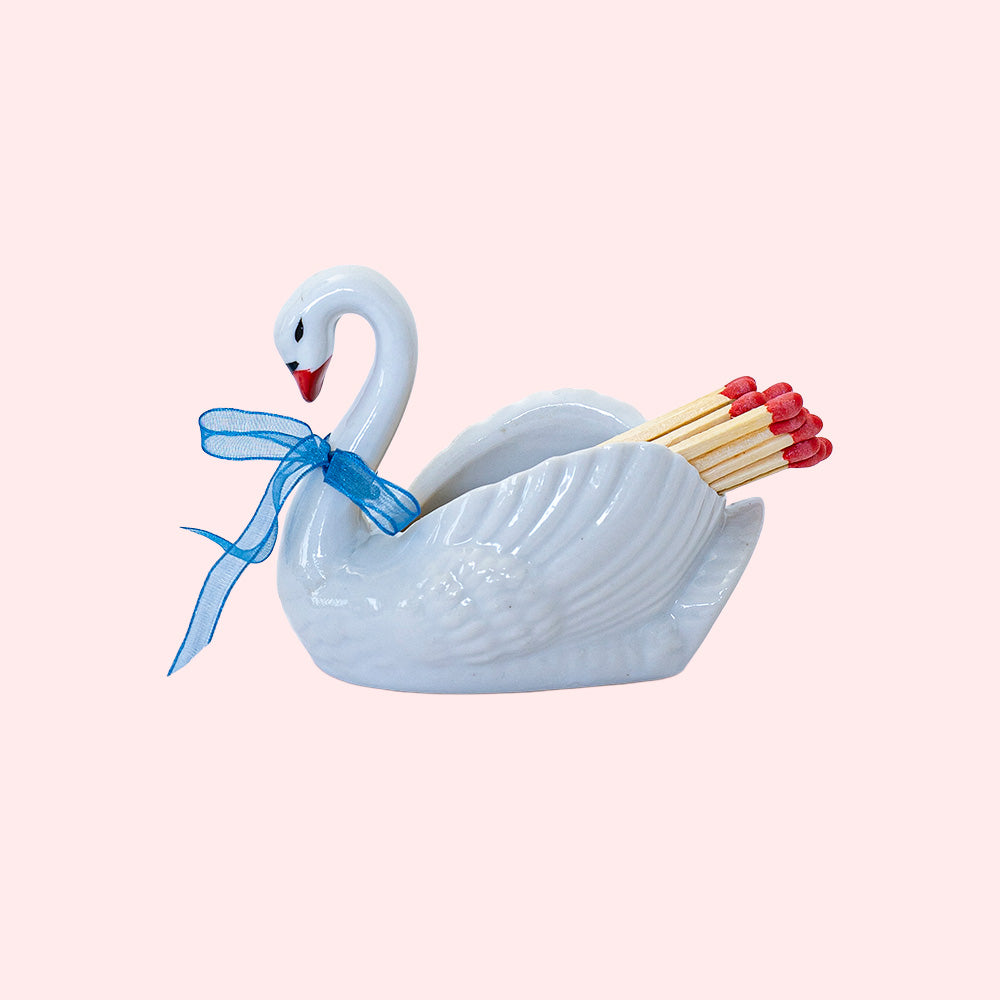 Second-hand ceramic, hollow swan figurine filled with 20 matches. It's wearing a blue organza ribbon.  