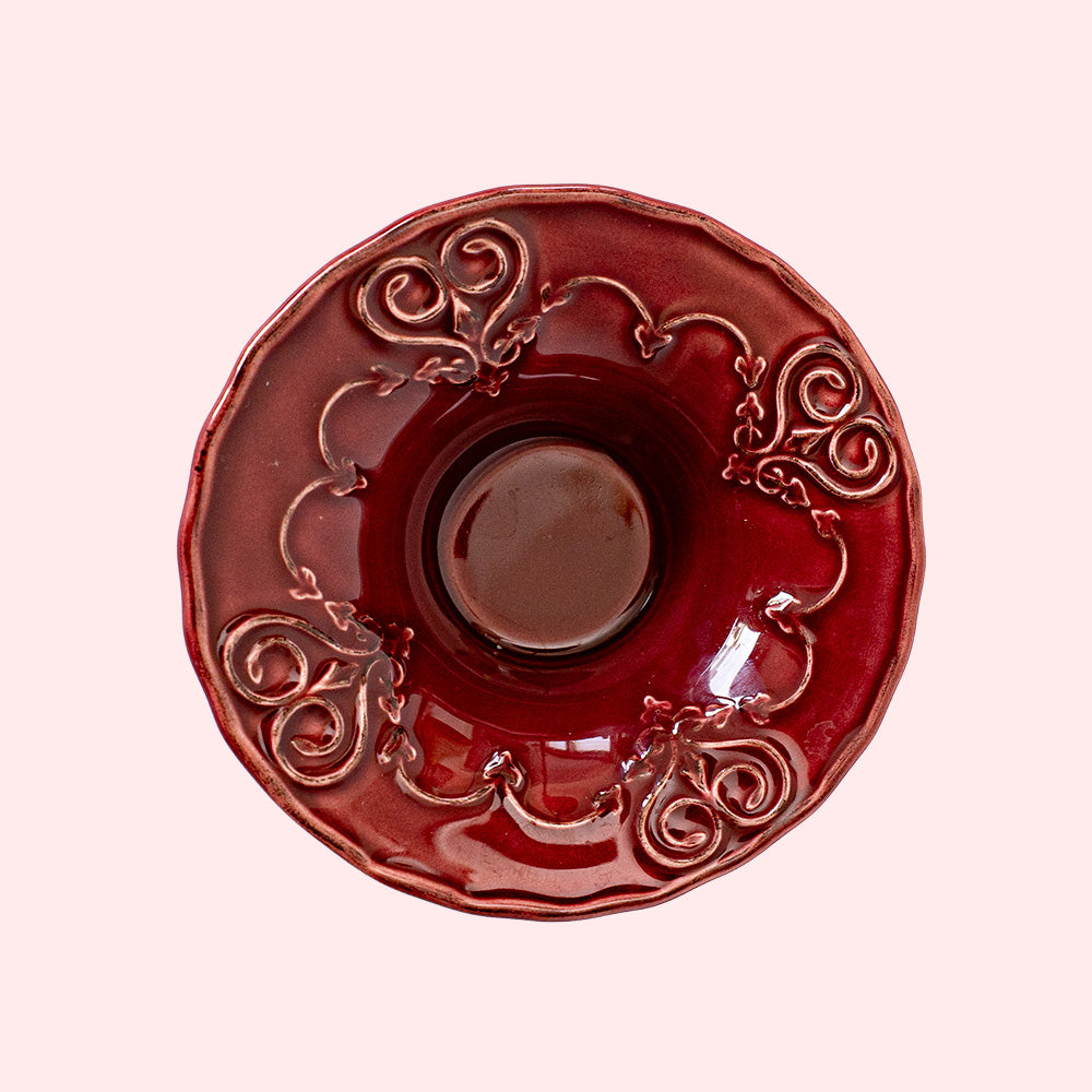 A burgundy colored tealight holder with intricate heart patterns.