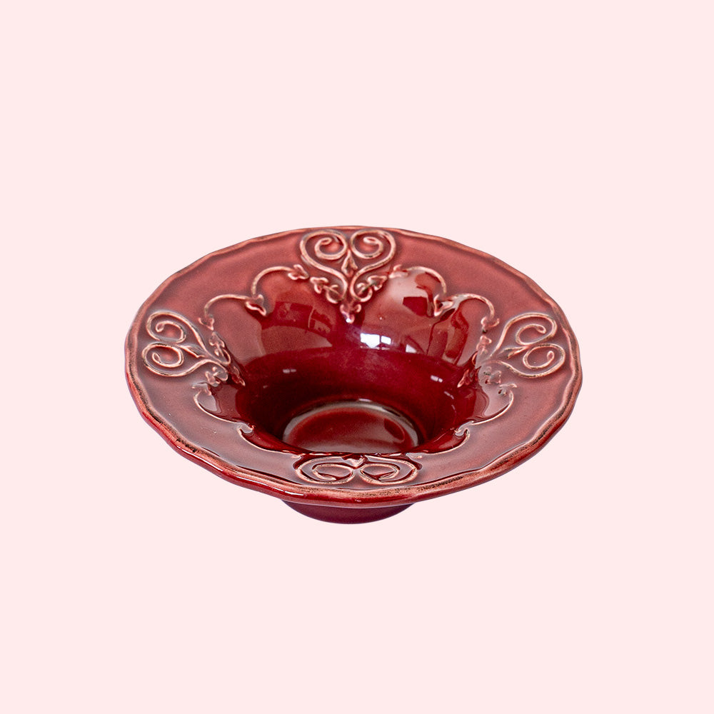 A burgundy colored tealight holder with intricate heart patterns.