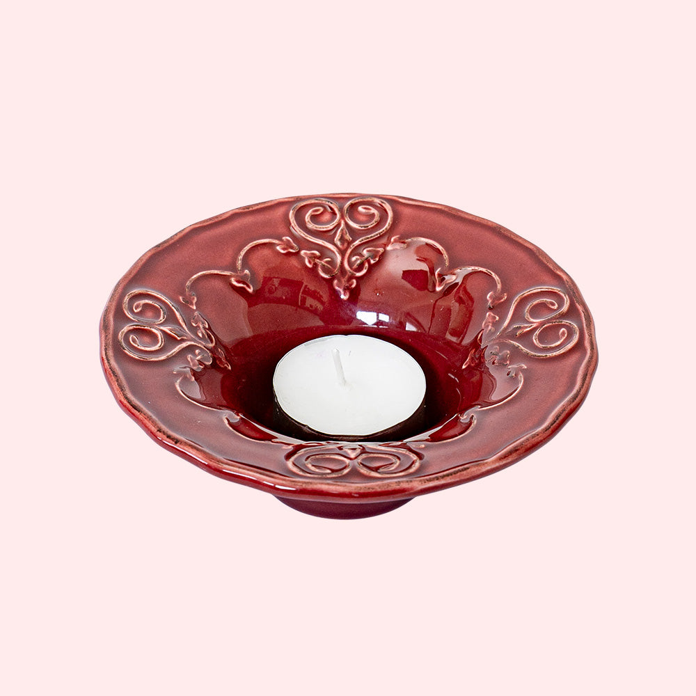 A burgundy colored tealight holder with intricate heart patterns.