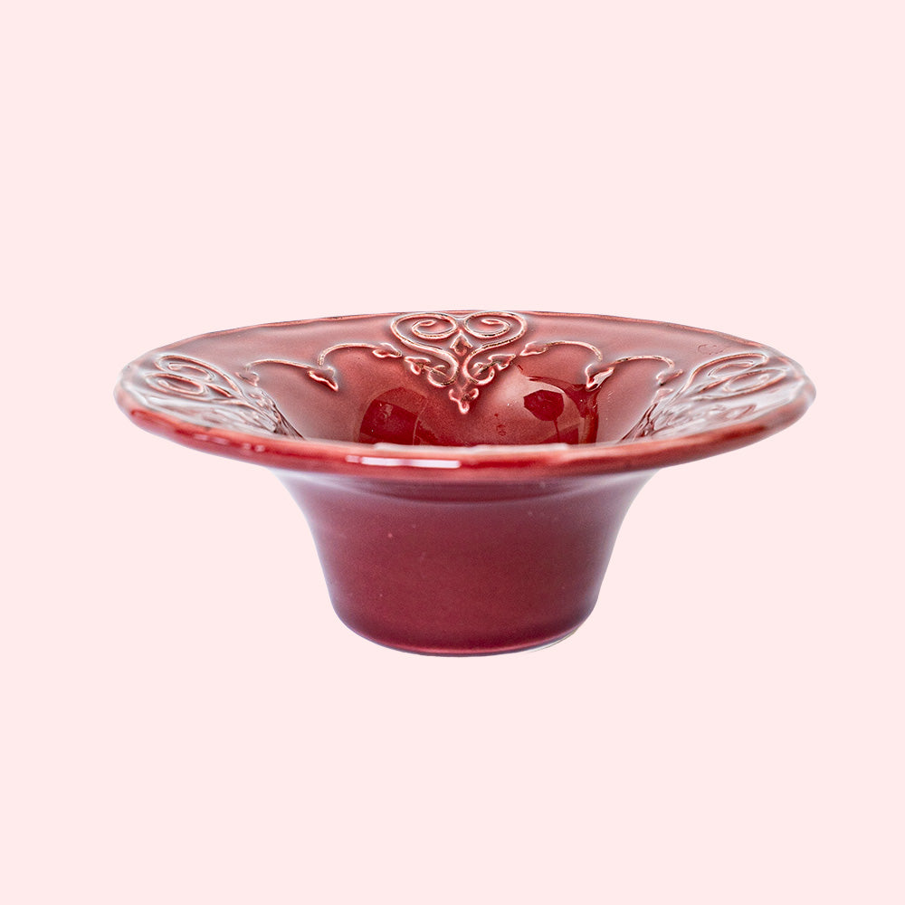 A burgundy colored tealight holder with intricate heart patterns.