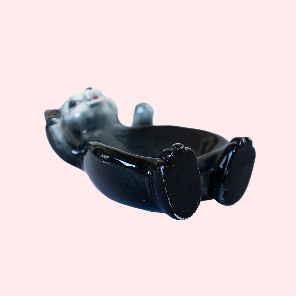 Second hand vintage trinket dish. It represents a black bear with a grey-white face, with his arms open. Seen from the side.